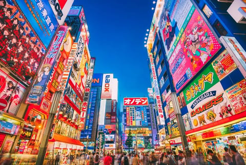 Vibrant street scene in Tokyo with colorful illuminated signs, crowded with pedestrians under a blue sky